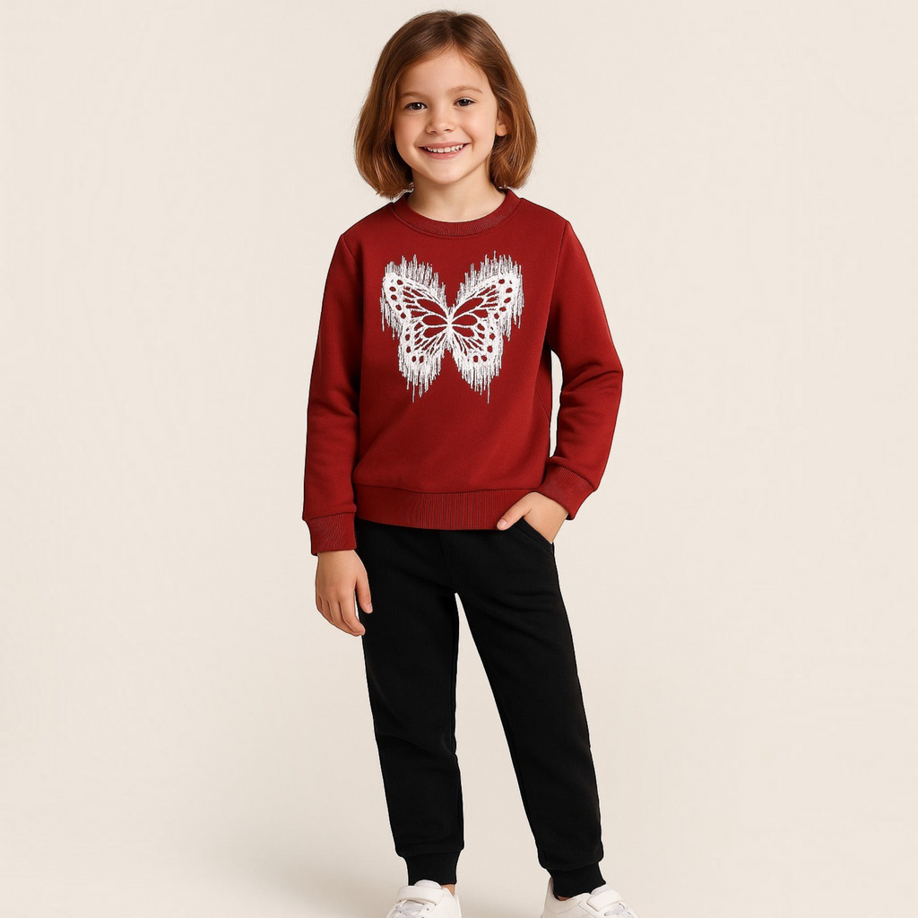 A young girl wearing a victor and jane red sweatshirt with a white glittery butterfly print and black joggers.
