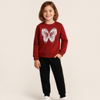 A young girl wearing a victor and jane red sweatshirt with a white glittery butterfly print and black joggers.