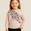 Young girl wearing a victor and jane light pink sweatshirt with a decorative sequin floral pattern on the chest.