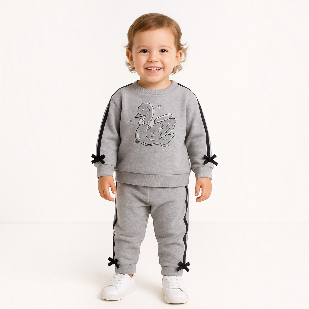 A toddler wearing a grey victor and jane 2-piece embroidered set with a swan graphic and black bow accents.