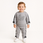 A toddler wearing a grey victor and jane 2-piece embroidered set with a swan graphic and black bow accents.