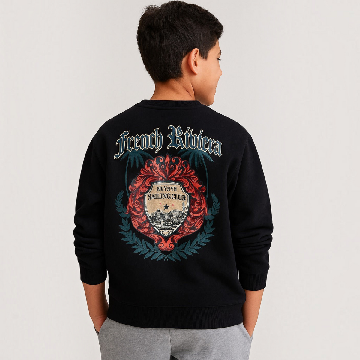 A boy wearing a black victor and jane graphic sweatshirt with a French Riviera sailing club print on the back.