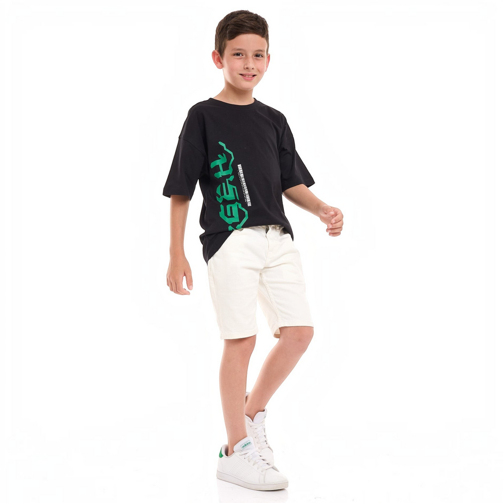 A young boy wearing a black victor and jane graphic t-shirt with green text and white denim shorts.