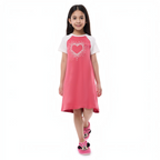 A young girl wearing a victor and jane pink and white short-sleeve pajama dress with a heart graphic and slippers.
