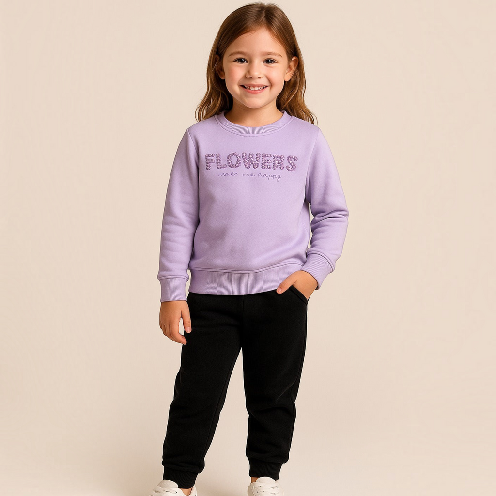 Young girl wearing a victor and jane light purple sweatshirt with floral text detail and black joggers
