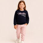 Young girl wearing a victor and jane navy blue sweatshirt with Malibu California graphic and light pink sweatpants
