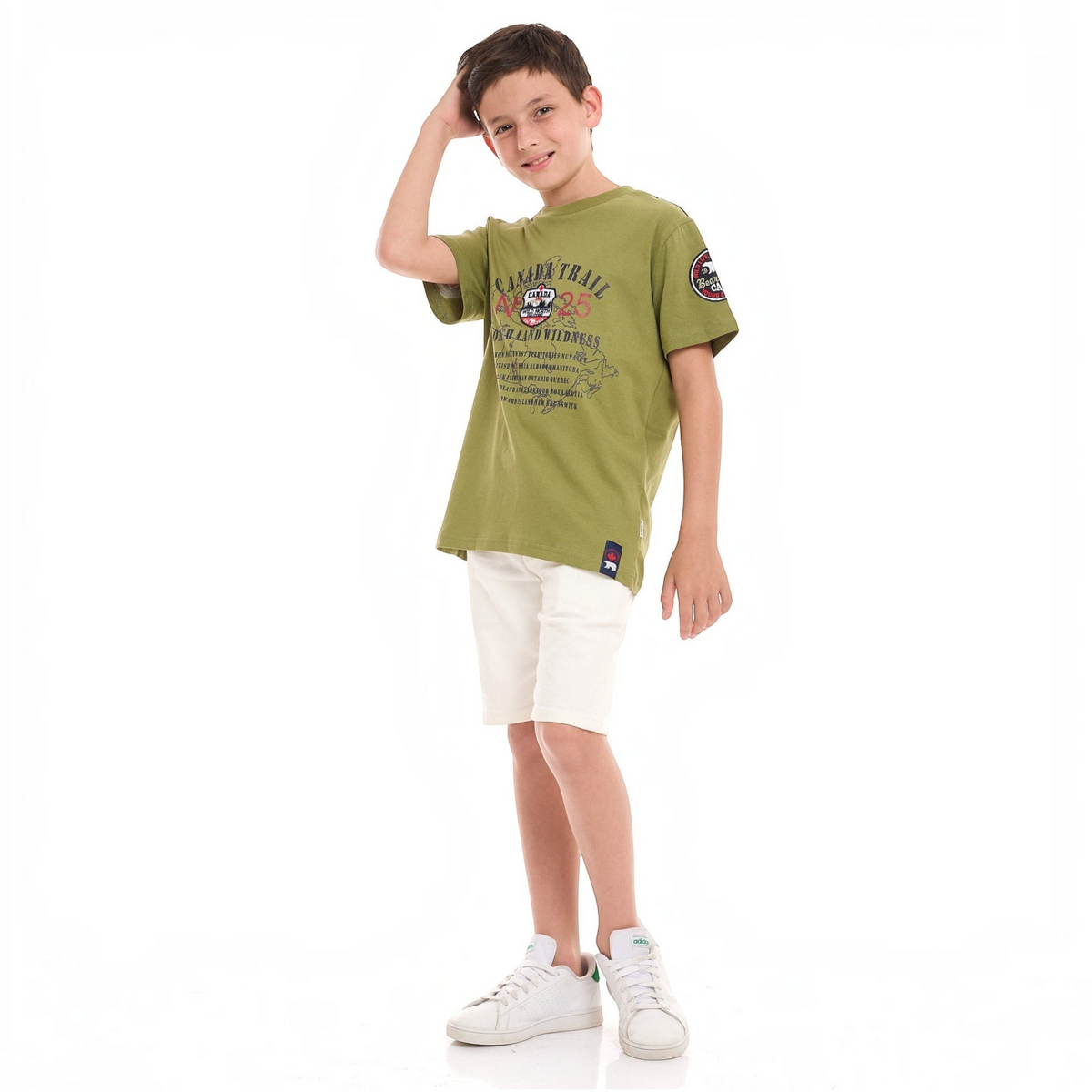 A young boy wearing a victor and jane olive green graphic t-shirt with Canada Trail print and white shorts.
