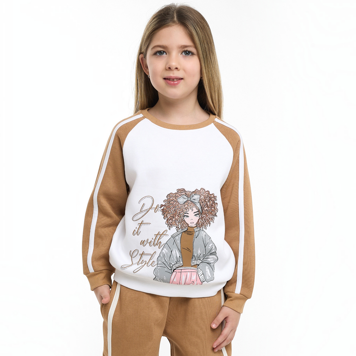Young girl wearing a victor and jane two-piece set with a white and tan graphic sweatshirt and matching tan joggers.