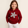 A young girl wearing a deep red victor and jane hoodie featuring a large embroidered silver and pink daisy flower