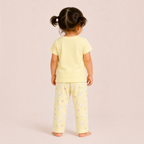 A young girl wearing a victor and jane yellow pyjama set with a cute bunny and floral print, back view.