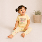 Toddler girl wearing a yellow victor and jane pyjama set with bunny and flower prints, sitting on a neutral floor.