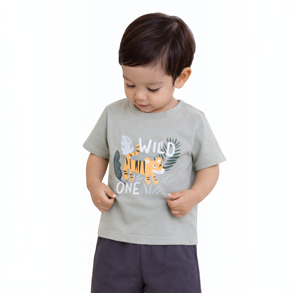A toddler boy wearing a sage green victor and jane t-shirt with a Wild One tiger graphic and dark grey shorts.
