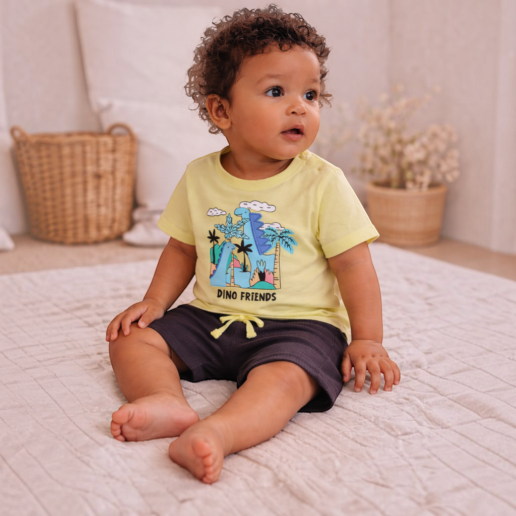victor and jane baby boy wearing a light yellow dinosaur print t-shirt and dark grey shorts sitting on a rug