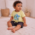 victor and jane baby boy wearing a light yellow dinosaur print t-shirt and dark grey shorts sitting on a rug