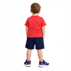 A young boy wearing a victor and jane red t-shirt and navy blue shorts, viewed from the back.