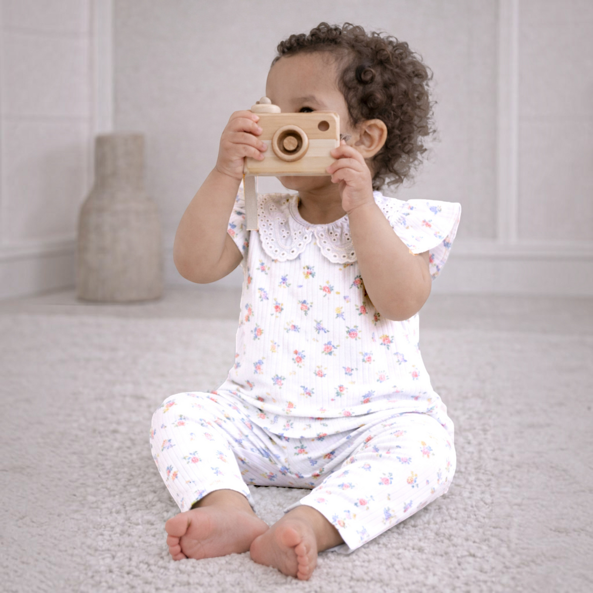 A toddler girl wearing a victor and jane floral print ribbed shirt set with a scalloped collar, playing with a toy.