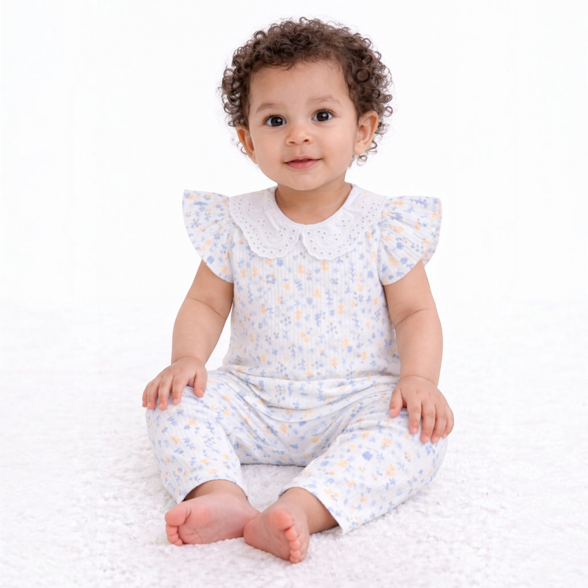 A baby girl wearing a victor and jane two-piece floral shirt set with flutter sleeves and a white eyelet collar.
