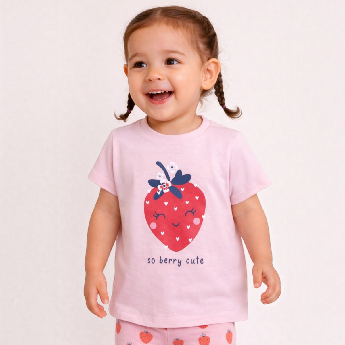 A toddler girl wearing a victor and jane light pink t-shirt with a strawberry graphic and matching strawberry leggings