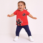 A toddler girl wearing a victor and jane red graphic t-shirt with floral print and navy blue leggings.