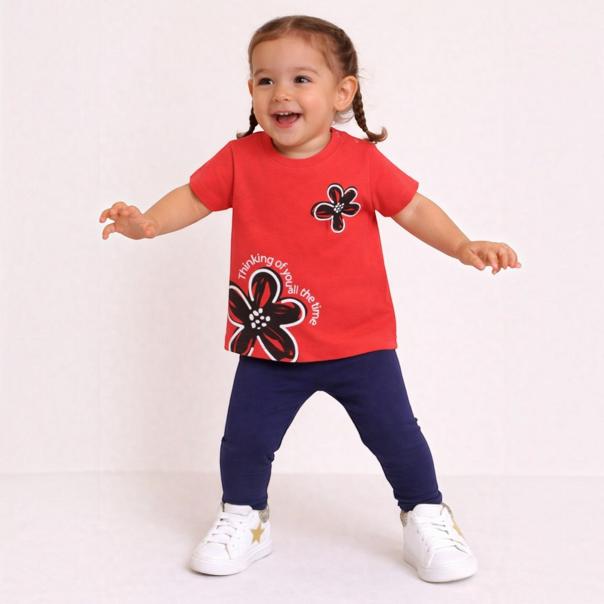 A toddler girl wearing a victor and jane red graphic t-shirt with floral print and navy blue leggings.
