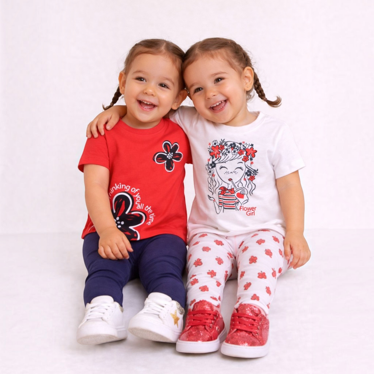 Two smiling girls wearing victor and jane graphic shirt sets with floral prints and leggings on a white background