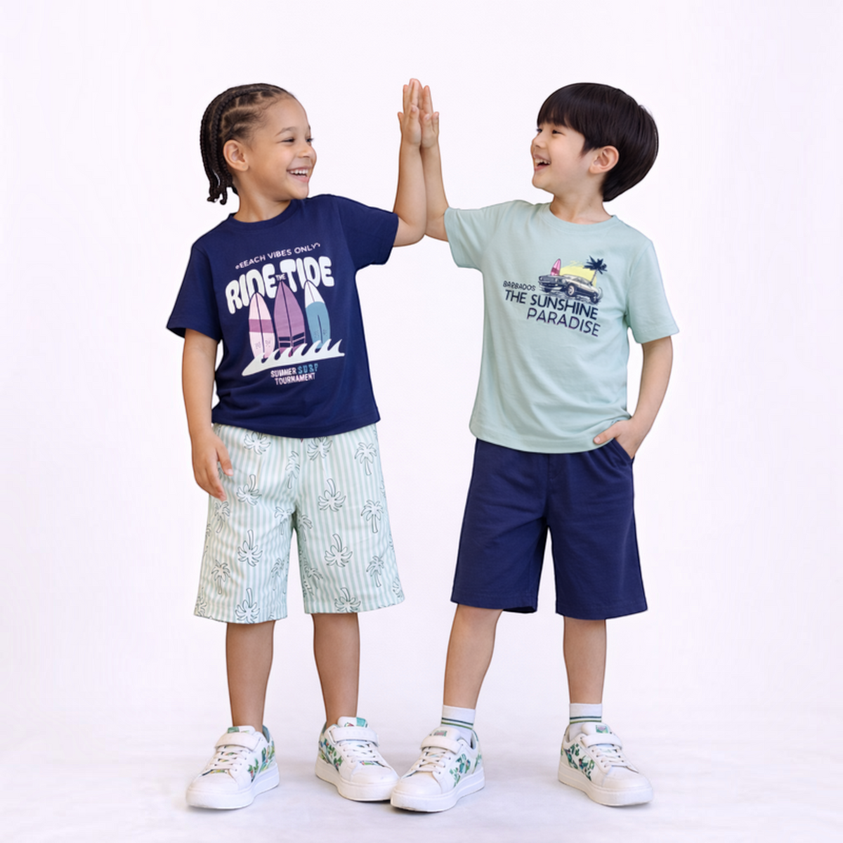 Two boys wearing victor and jane graphic t-shirts and shorts, high-fiving in a studio setting.