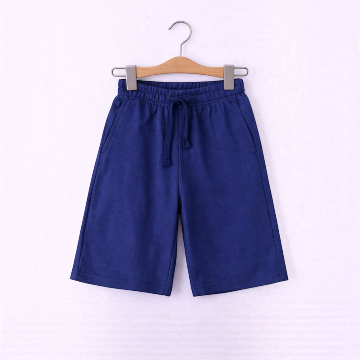 victor and jane boys blue cotton jersey shorts with an elastic drawstring waistband hanging on a wooden hanger