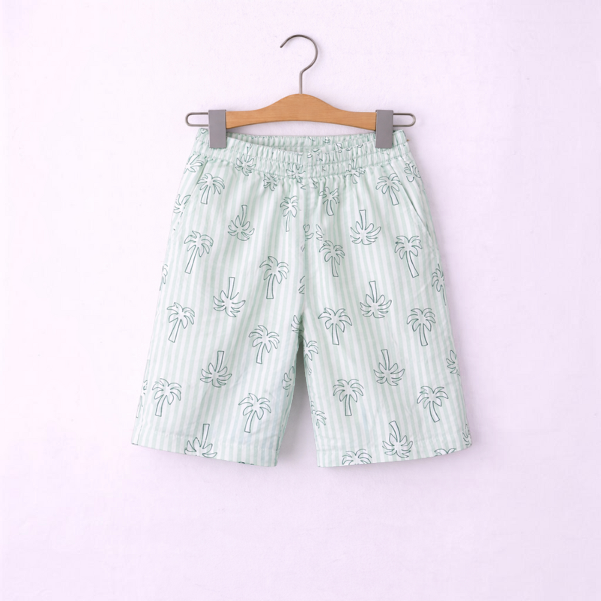 victor and jane boys light green striped shorts with white palm tree print hanging on a wooden hanger