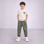 A young boy wearing a victor and jane cream graphic t-shirt and olive green joggers with matching text prints.