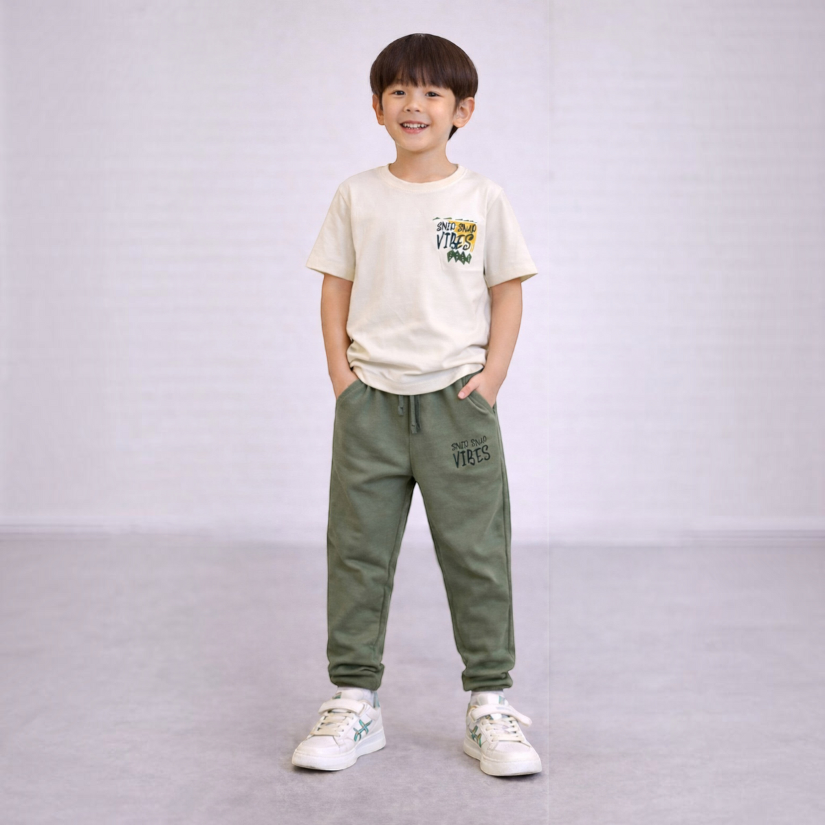 A young boy wearing a victor and jane cream graphic t-shirt and olive green joggers with matching text prints.