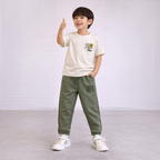 Young boy wearing a victor and jane cream graphic t-shirt and olive green joggers giving a thumbs up