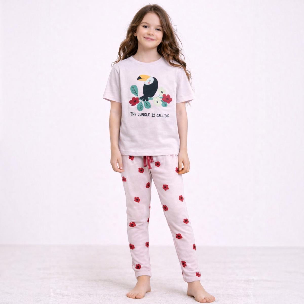 A young girl wearing a victor and jane light pink graphic t-shirt with a toucan print and matching floral trousers.