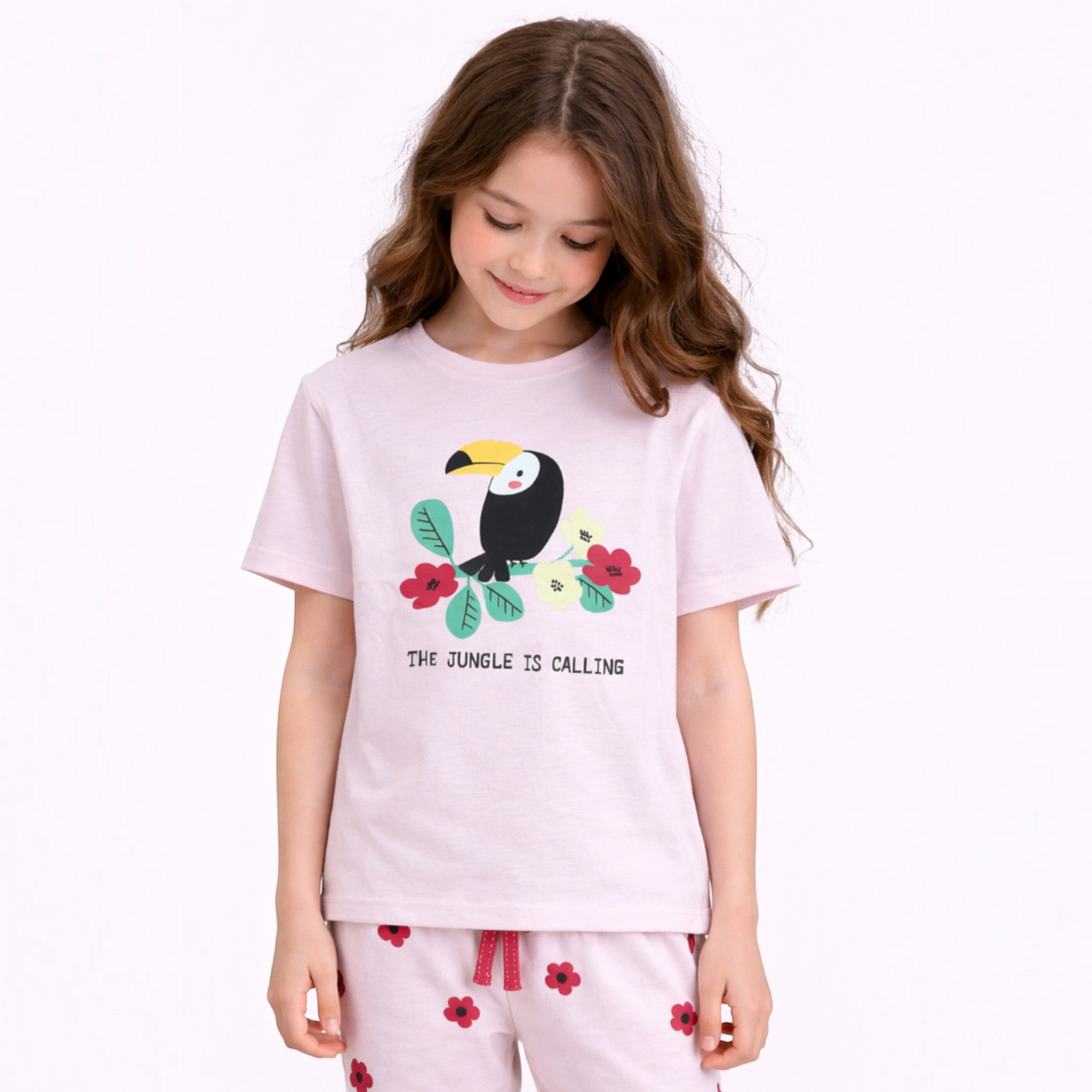 A young girl wearing a light pink victor and jane graphic t-shirt featuring a toucan and The Jungle Is Calling text.