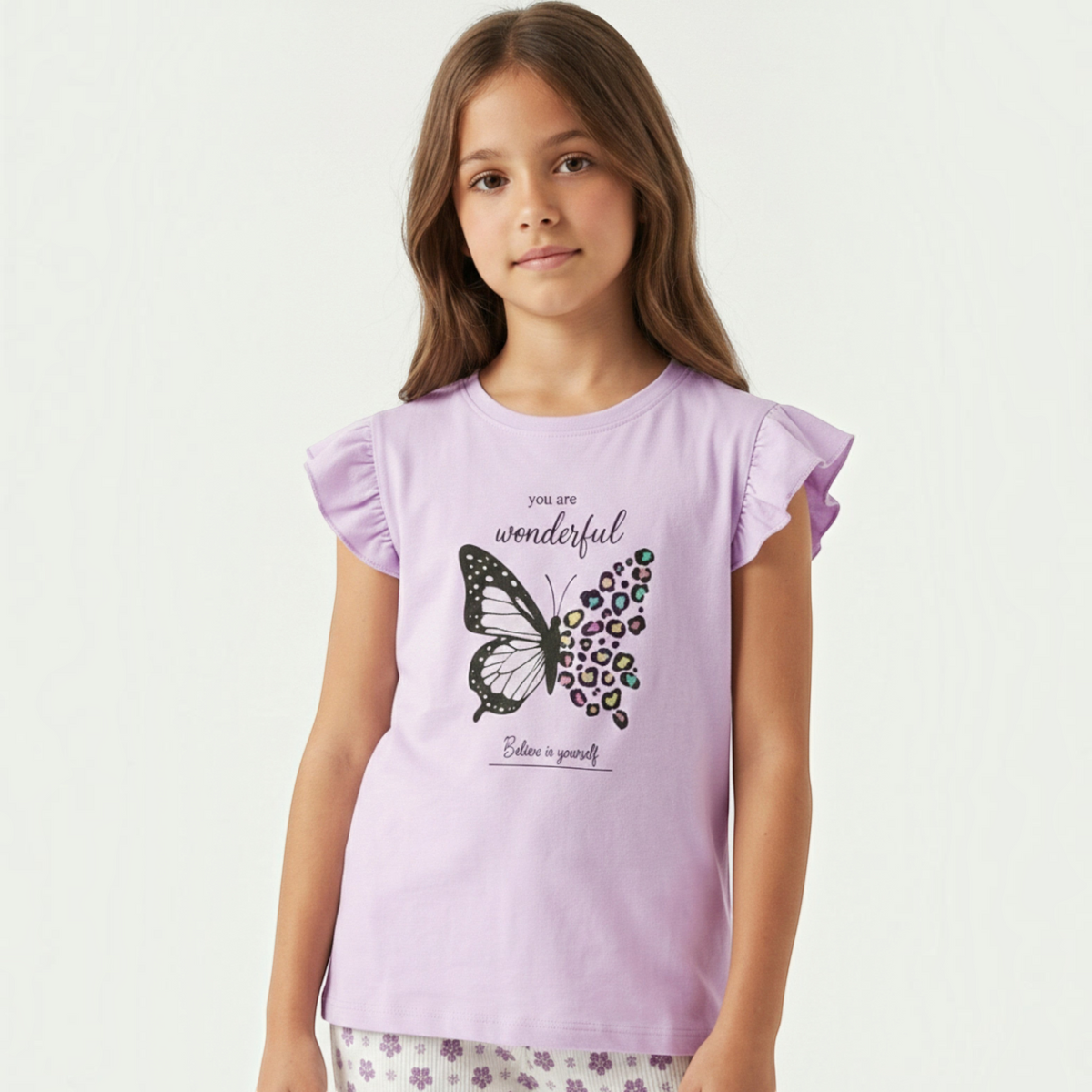 Young girl wearing a light purple victor and jane graphic pyjama top with a butterfly print and ruffled sleeves.