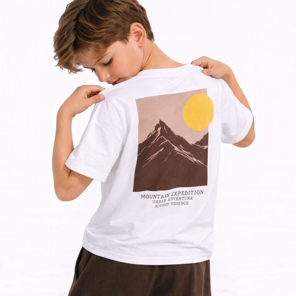 A boy wearing a white victor and jane graphic t-shirt featuring a mountain and sun print on the back