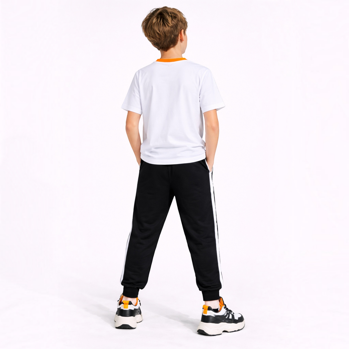 A young boy wearing a victor and jane white t-shirt with orange trim and black joggers with white side stripes.