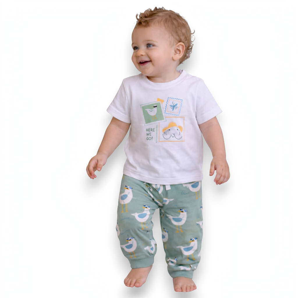 A smiling toddler wearing a victor and jane white graphic t-shirt with a travel-themed print and seagull print pants.