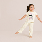 A young girl wearing a victor and jane cream cartoon t-shirt and floral pajama pants, smiling and posing.
