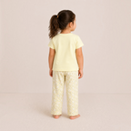 A young girl wearing a victor and jane pale yellow t-shirt and matching floral print pajama pants from behind.