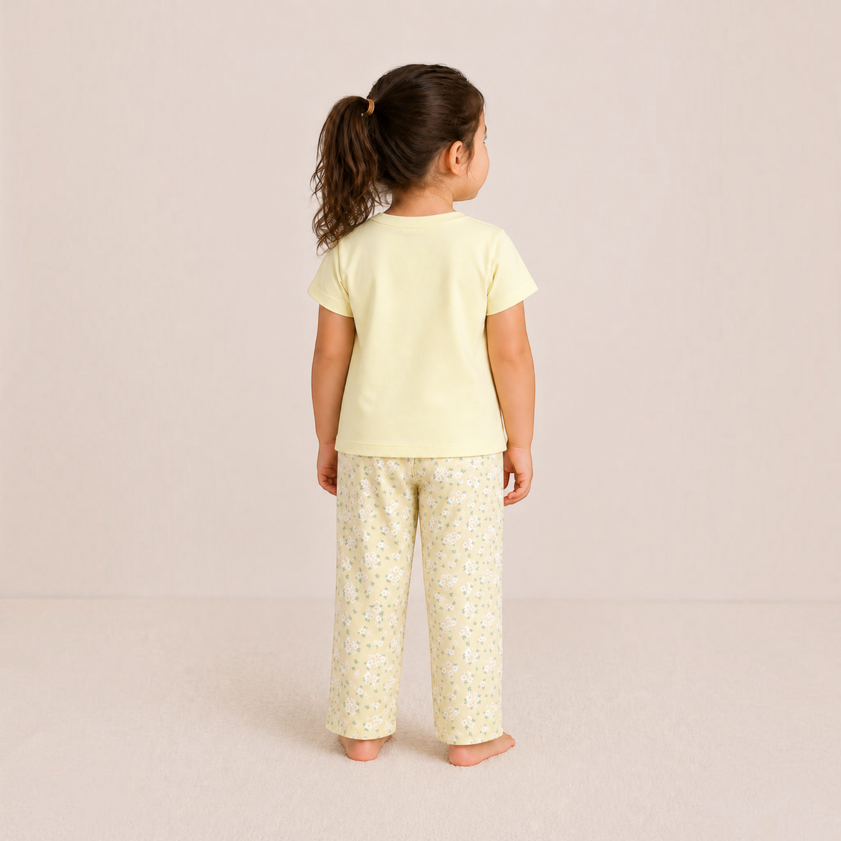 A young girl wearing a victor and jane pale yellow t-shirt and matching floral print pajama pants from behind.