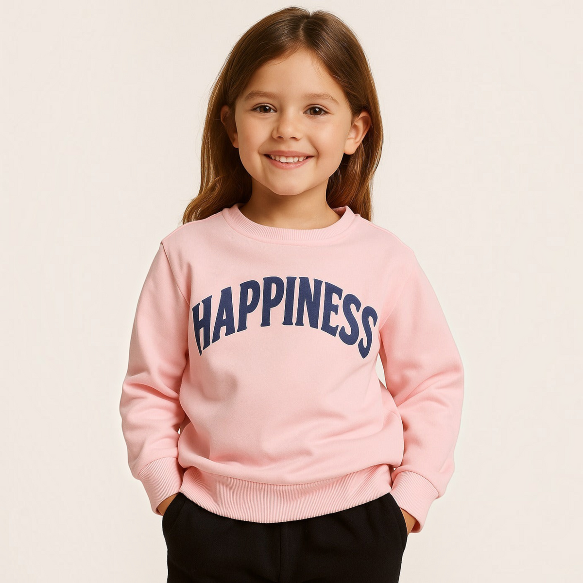 A young girl smiling while wearing a light pink victor and jane EURA sweatshirt with HAPPINESS printed in navy blue.
