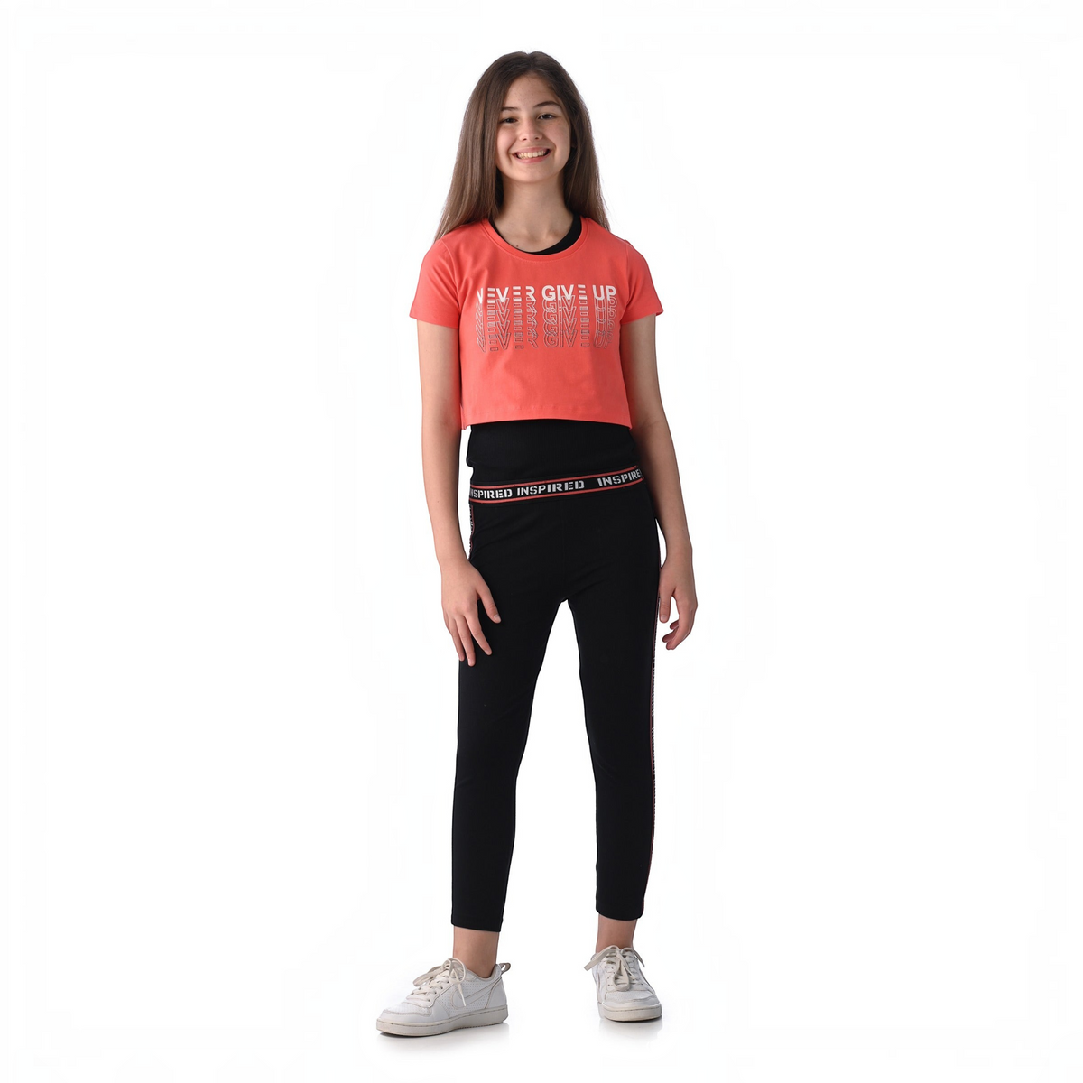 A smiling girl wearing a victor and jane coral crop top with Never Give Up text and black leggings with logo trim.
