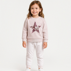 Young girl wearing a victor and jane pale pink sweatshirt featuring a large sparkling sequin star design