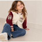 Young girl wearing a victor and jane cream and maroon varsity jacket with Los Angeles graphics and striped ribbed trim