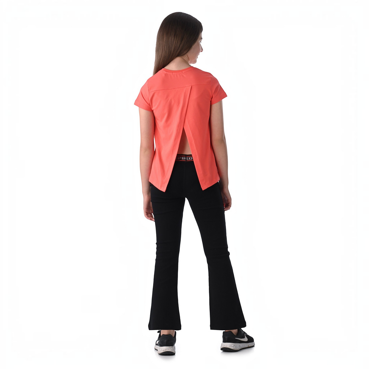A girl wearing a victor and jane coral short-sleeve top with an open back design and black flared trousers.
