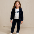 Young girl wearing a victor and jane navy glitter velour hoodie, white graphic tee, and matching jogger pants set.