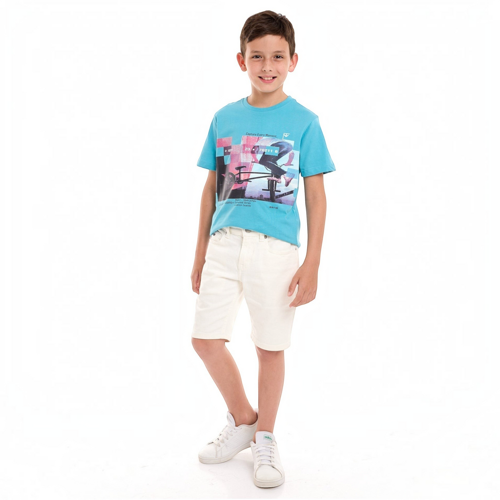 Young boy wearing a bright blue victor and jane graphic t-shirt with white shorts and sneakers against white background