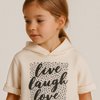 Young girl wearing a victor and jane cream short-sleeved hoodie with a black leopard print live laugh love graphic