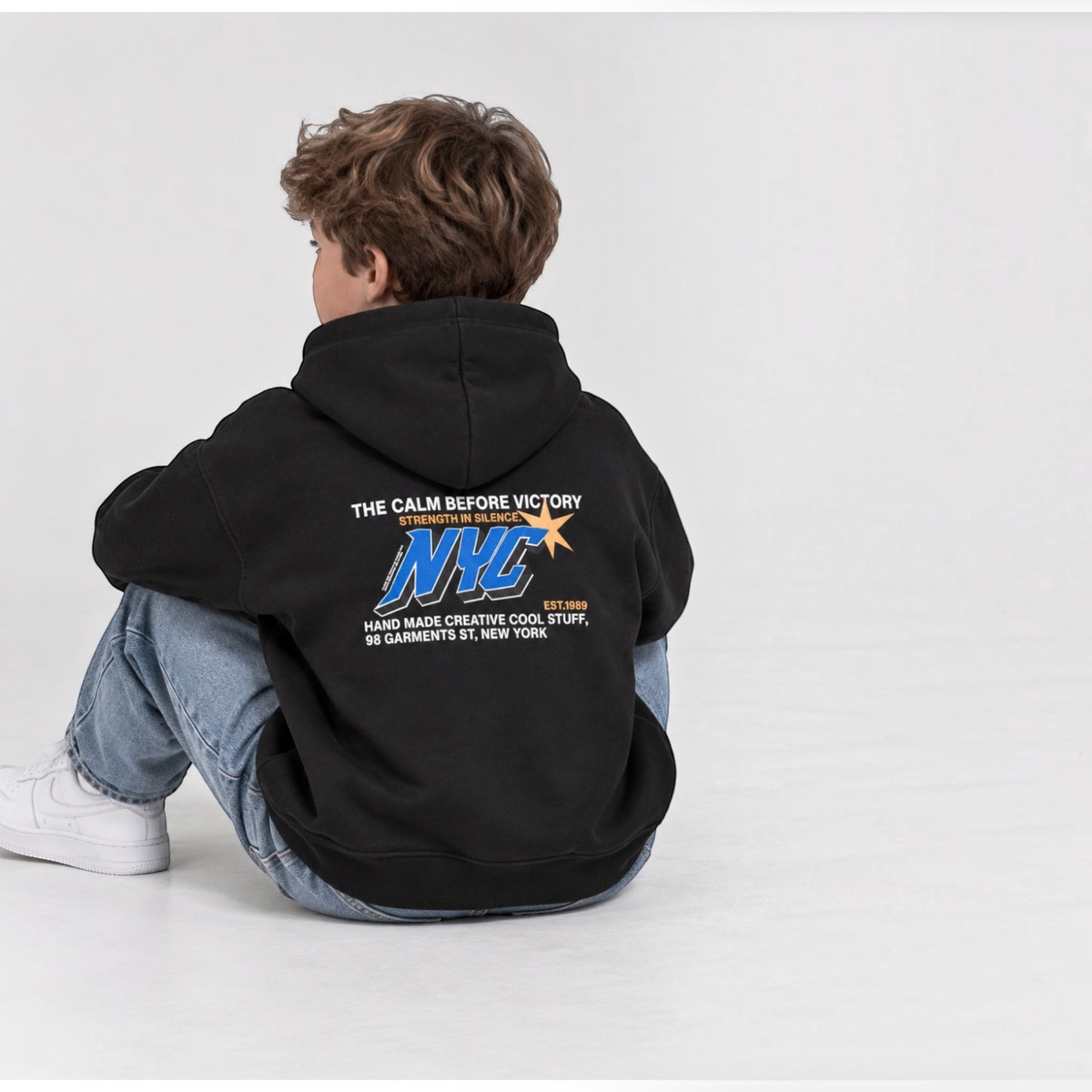 victor and jane boys black fleece hoodie with NYC graphic print on back worn by a boy sitting on the floor