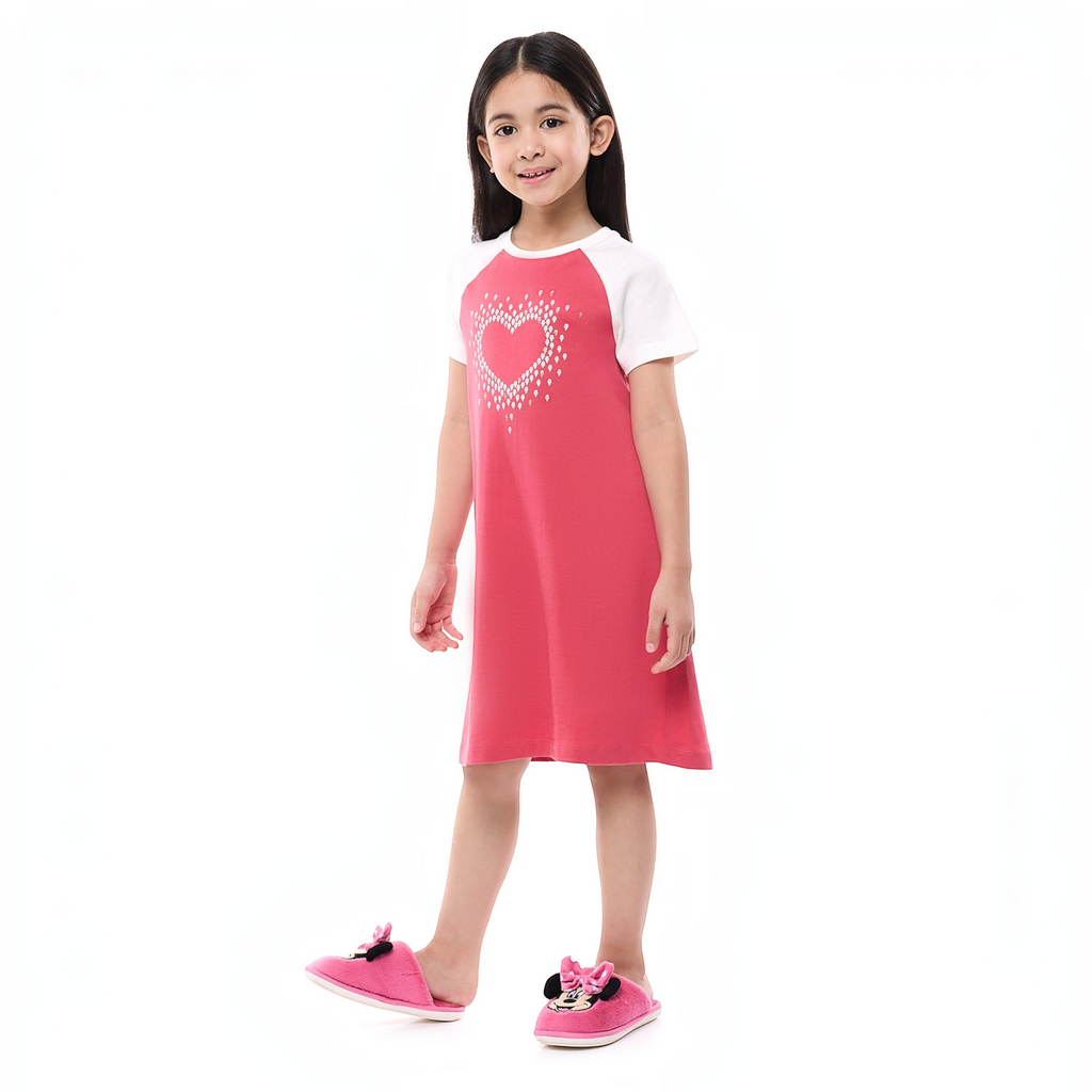 Young girl wearing a victor and jane pink and white short-sleeve pajama dress with a heart graphic and plush slippers